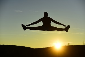 Sportliche erson macht einen Spagatsprung in die Luft vor dem Sonnenuntergang